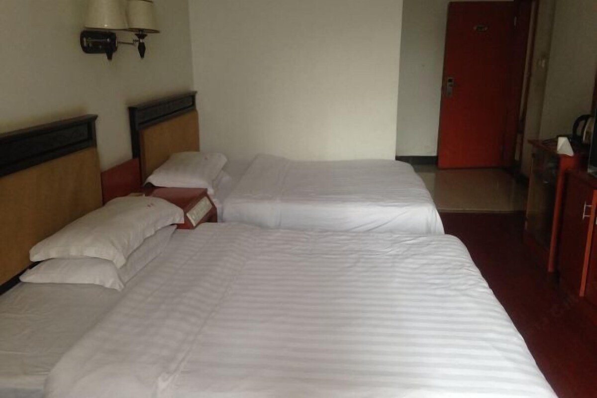 A hotel room with two beds, a red door, and a wall-mounted lamp.