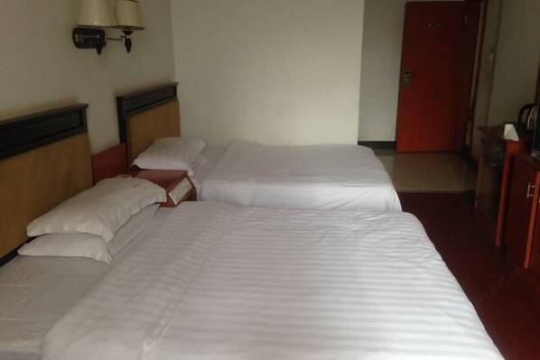 A hotel room with two beds, a red door, and a wall-mounted lamp.