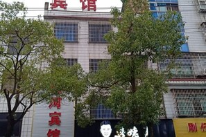 Un immeuble à plusieurs étages, une enseigne avec des caractères chinois et un arbre devant.