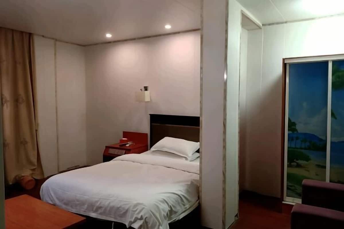 A hotel room with a bed, a nightstand, a lamp, a red chair, and a sliding door with a view of a landscape.