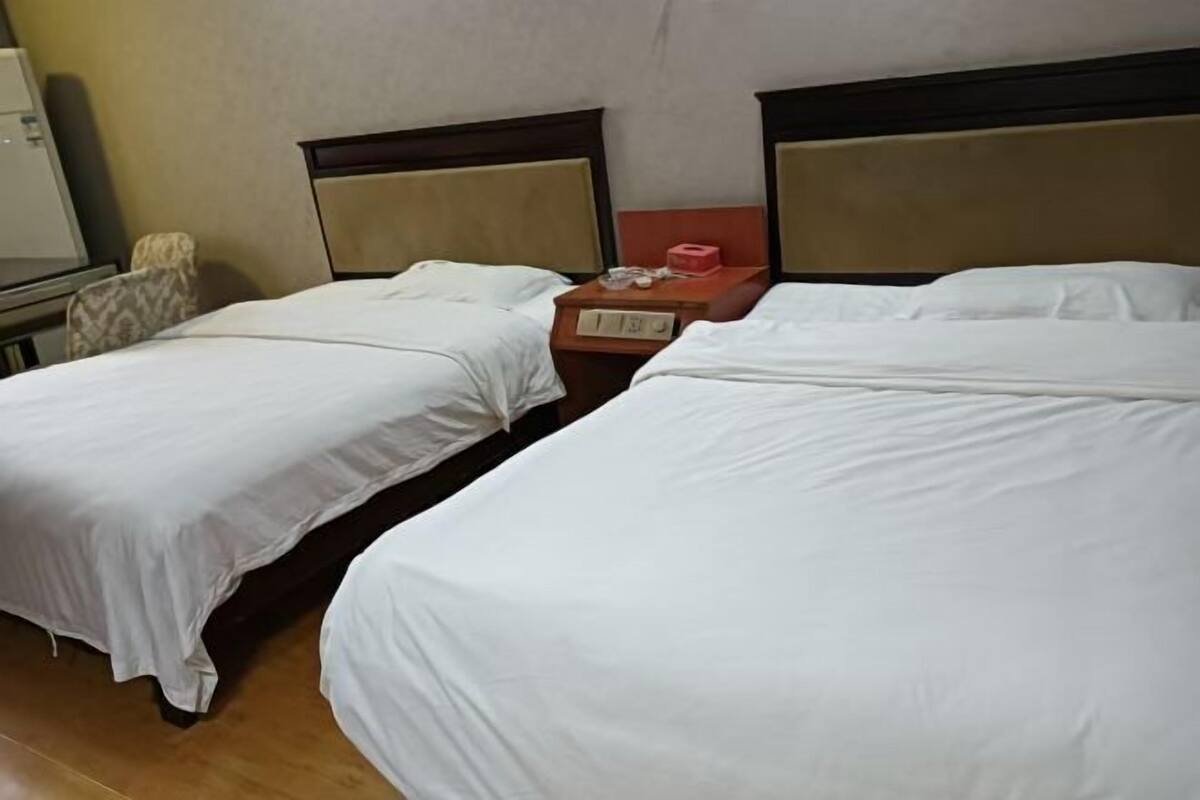 A hotel room with two single beds, a small table with a chair, and a nightstand with a lamp.