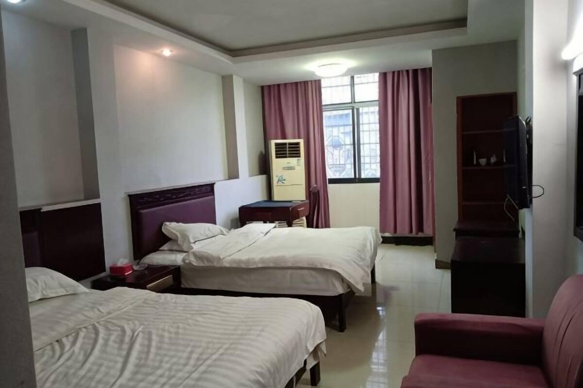 A hotel room with two beds, a desk, a chair, a TV, and a window with curtains.