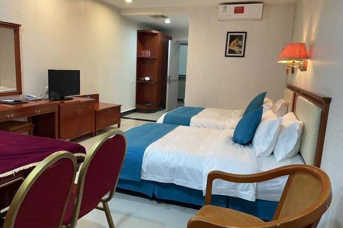 A hotel room with two beds, a desk with a computer, a chair, a TV, and a wardrobe.