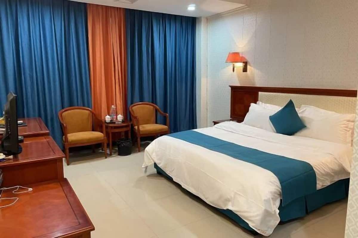 A hotel room with a bed, two chairs, a desk, and a lamp.
