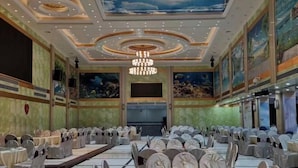 A banquet hall with round tables and chairs, a chandelier, and murals on the walls. - Yin Xi Hotel (Huidong)