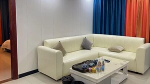 A white leather sofa with two pillows, a coffee table with various items, and a room with white walls and a door. - Yin Xi Hotel (Huidong)