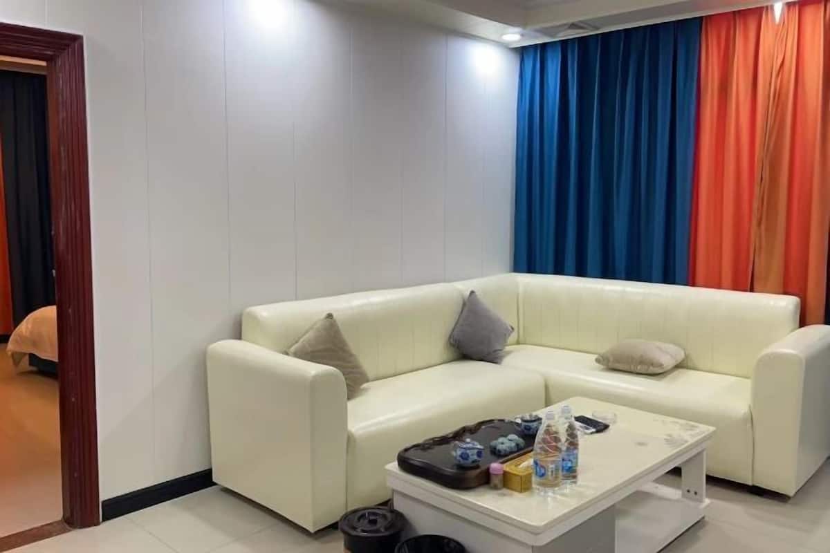 A white leather sofa with two pillows, a coffee table with various items, and a room with white walls and a door.