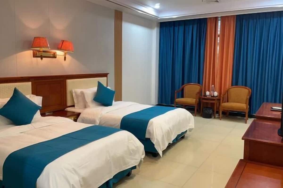 A hotel room with two beds, a desk, two chairs, and a small table.
