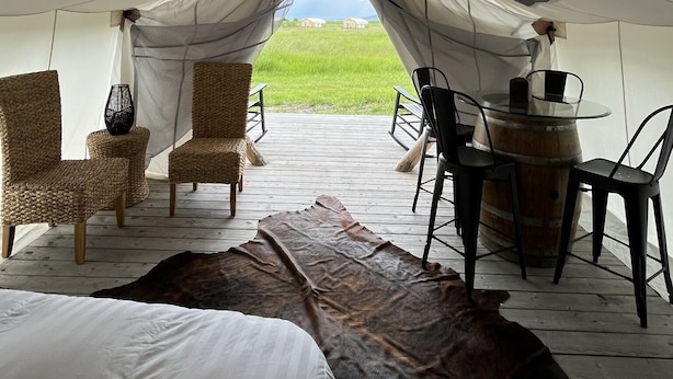 A tent with a wooden deck, wicker chairs, a glass table, and a leather rug.