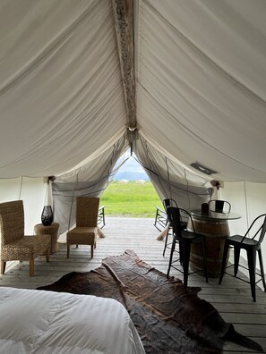 A tent with a wooden deck, wicker chairs, a glass table, and a leather rug. - Heritage Ranch 'Buckskin' Glamping Tent (5) (Bozeman)
