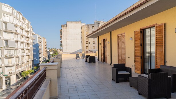 Ein Balkon mit Gartenmöbeln, gefliestem Boden und Blick auf die umliegenden Gebäude.