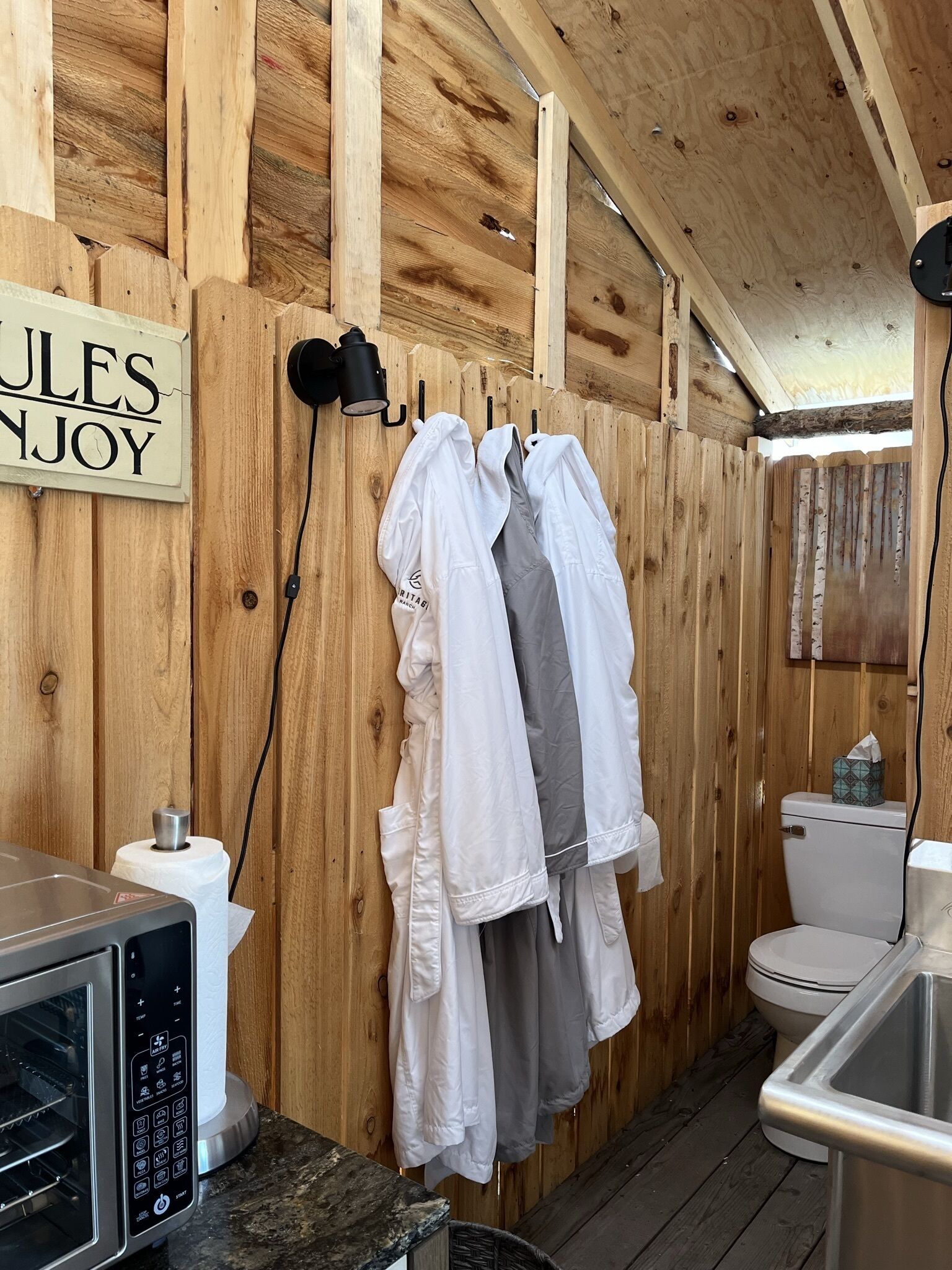 Un intérieur en bois avec une enseigne indiquant « JULES ENJOY », un four à micro-ondes, des toilettes et des vêtements suspendus sur un portant.