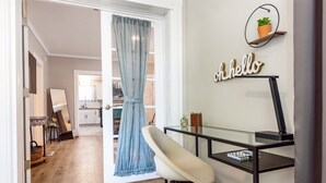 Une pièce moderne avec un bureau en verre, une chaise, un panneau indiquant « Bonjour », une plante en pot et une vue sur la cuisine.