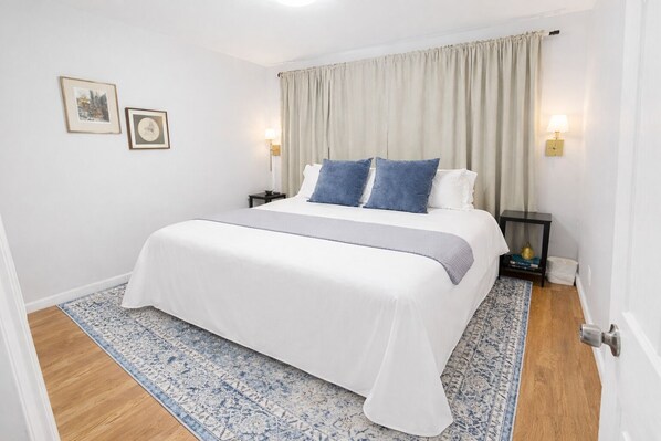 Un dormitorio ordenado con una cama grande, un tapete con estampado azul y blanco, y dos mesitas de noche con lámparas.