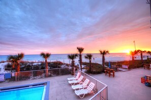 Un área de piscina frente a la playa con sillones de descanso y vistas a la puesta de sol sobre el océano.