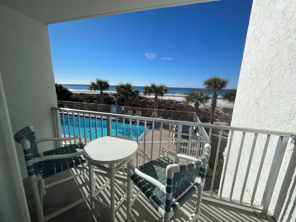 A balcony with a pool, chairs, and a view of the beach and ocean.