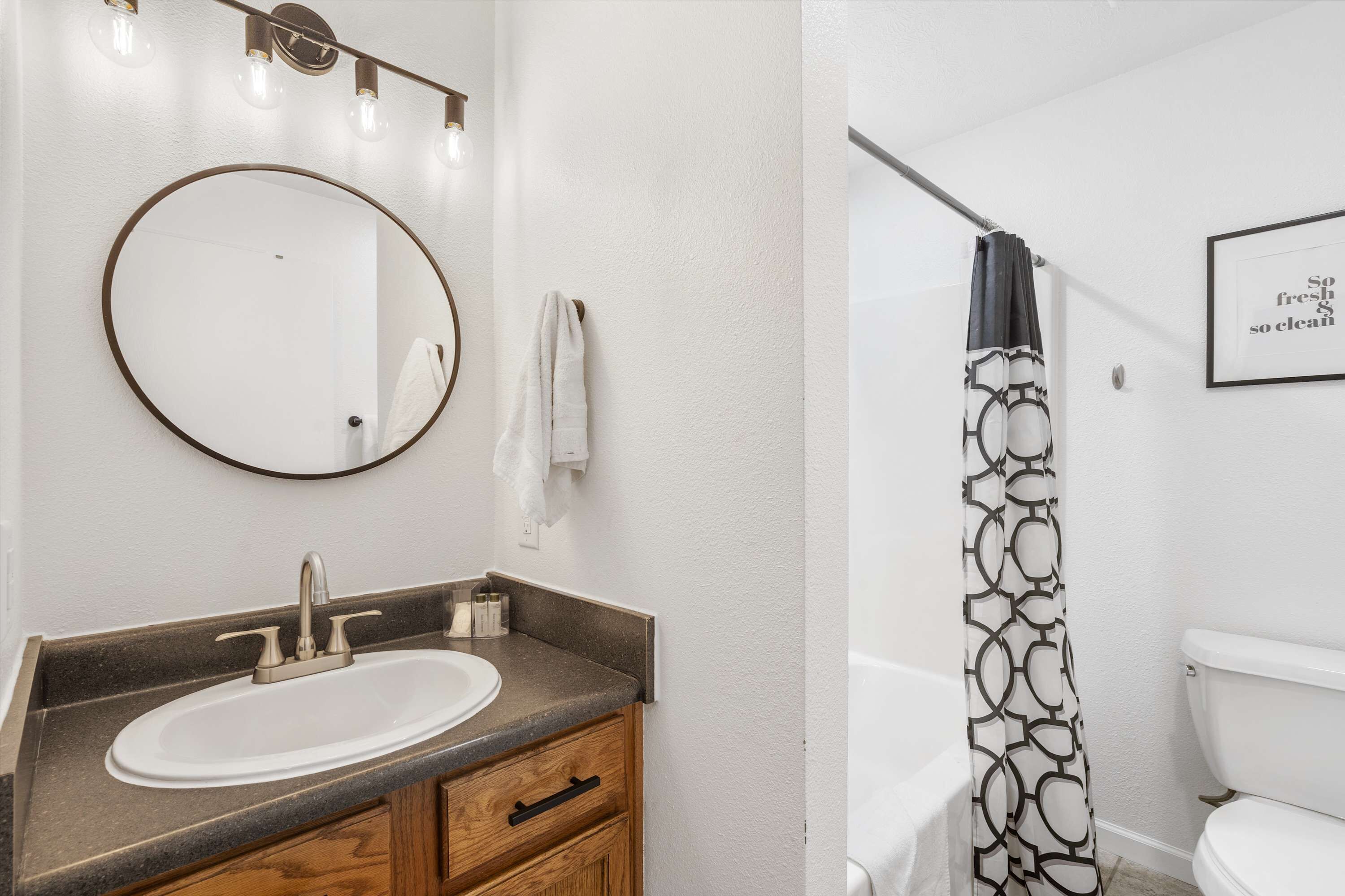 A bathroom with a round mirror, a sink with a faucet, a towel hanging on the wall, and a shower curtain with a geometric pattern.