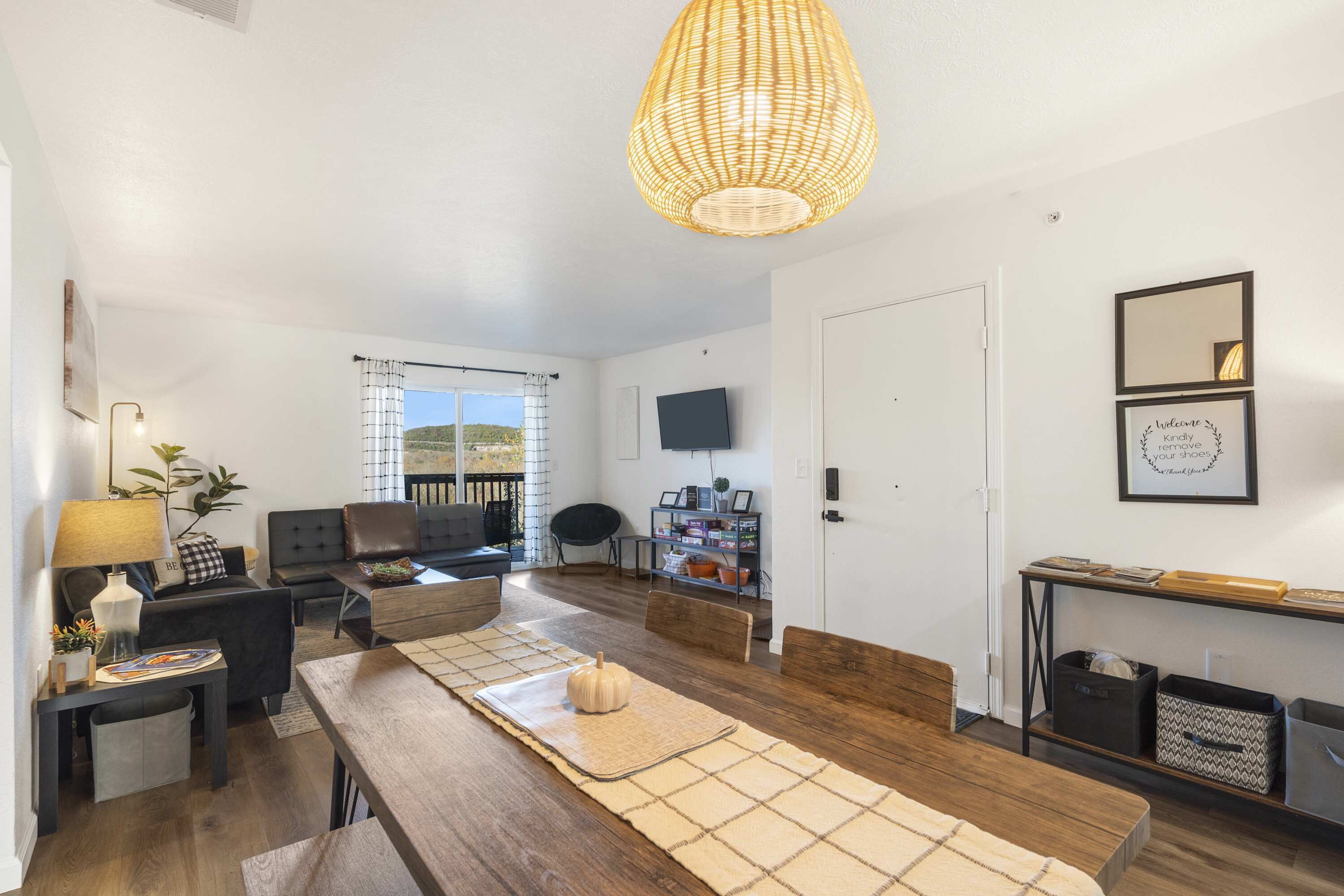 A modern living room with a wooden dining table, sofa, and a large woven light fixture.