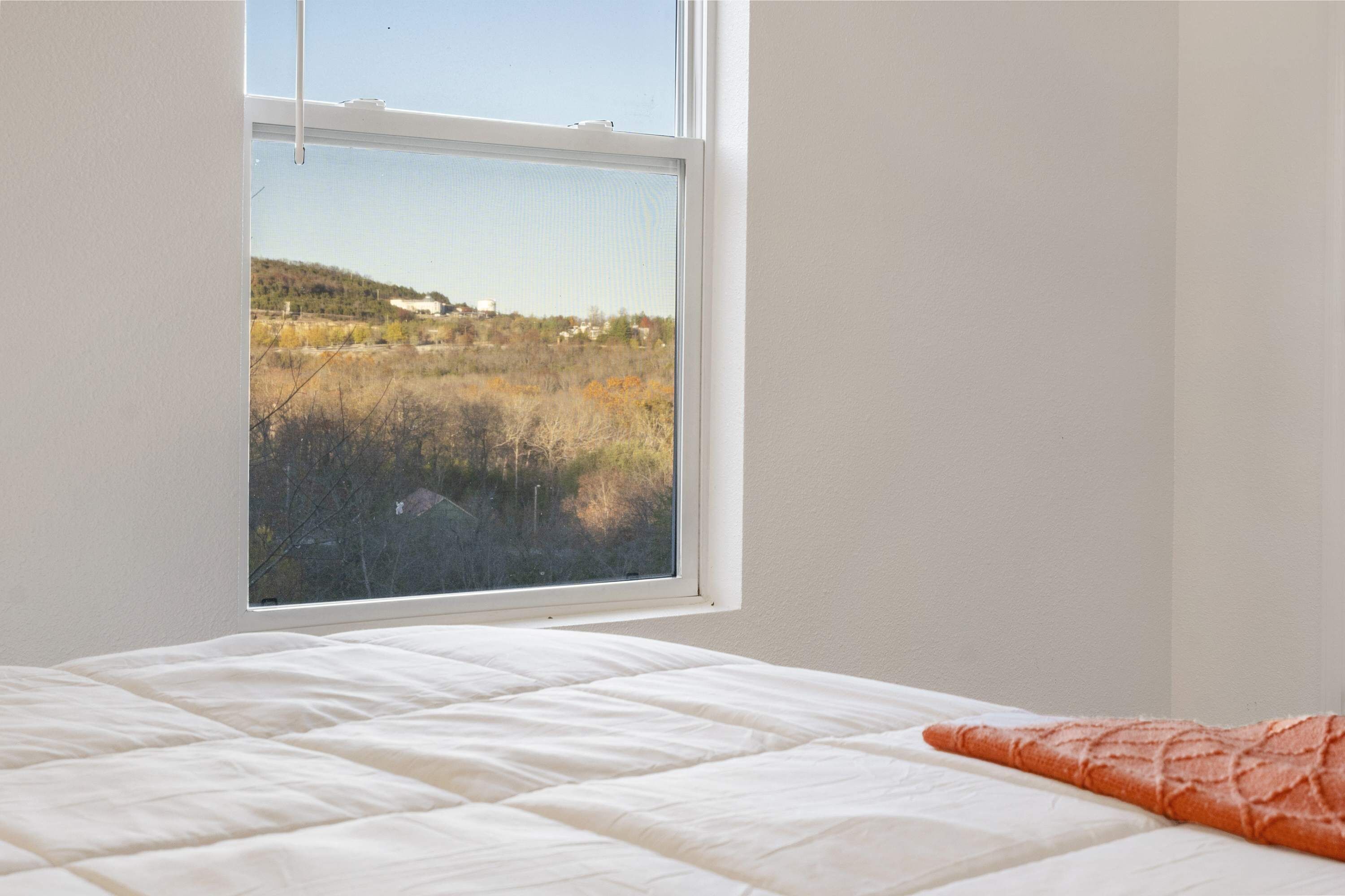 A bedroom with a bed, a window, and a view of a field.