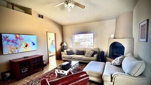 Ein Wohnzimmer mit Fernseher, einer Couch, einem roten Sessel, einem Couchtisch, einem Kamin und einem Deckenventilator.
