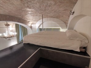 Quarto moderno com cama grande, lustre e teto curvo singular.