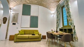 Uma sala de estar acolhedora com um sofá verde, uma mesa de jantar com cadeiras e uma área de cozinha com janela.