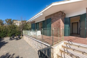 A two-story building with a balcony, stone wall, and a paved area with two lounge chairs. - 3169 Villa Enea by Barbarhouse (Porto Cesareo)