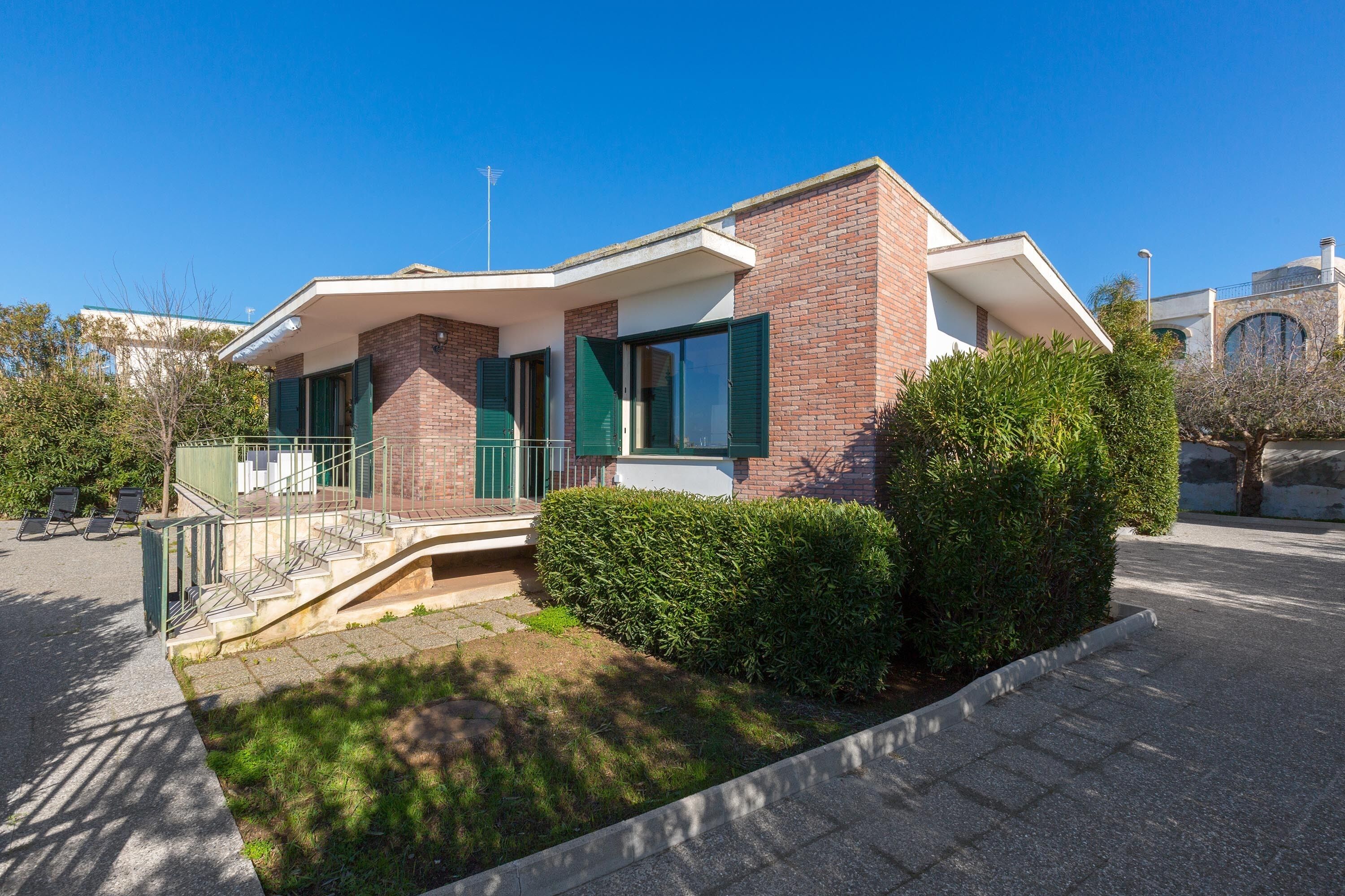 A modern two-story building with a brick facade, green shutters, and a small front garden.