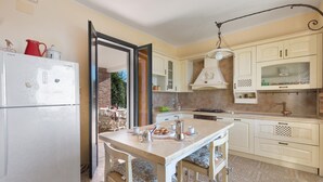 A kitchen with a white refrigerator, wooden dining table, and cabinets. - 3169 Villa Enea by Barbarhouse (Porto Cesareo)