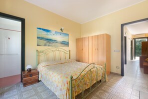 A bedroom with a bed, a wooden wardrobe, a painting on the wall, and a nightstand with a lamp. - 3169 Villa Enea by Barbarhouse (Porto Cesareo)
