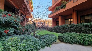 Pátio com calçada de azulejos, rodeado por vegetação exuberante e frutos vermelhos nas árvores.