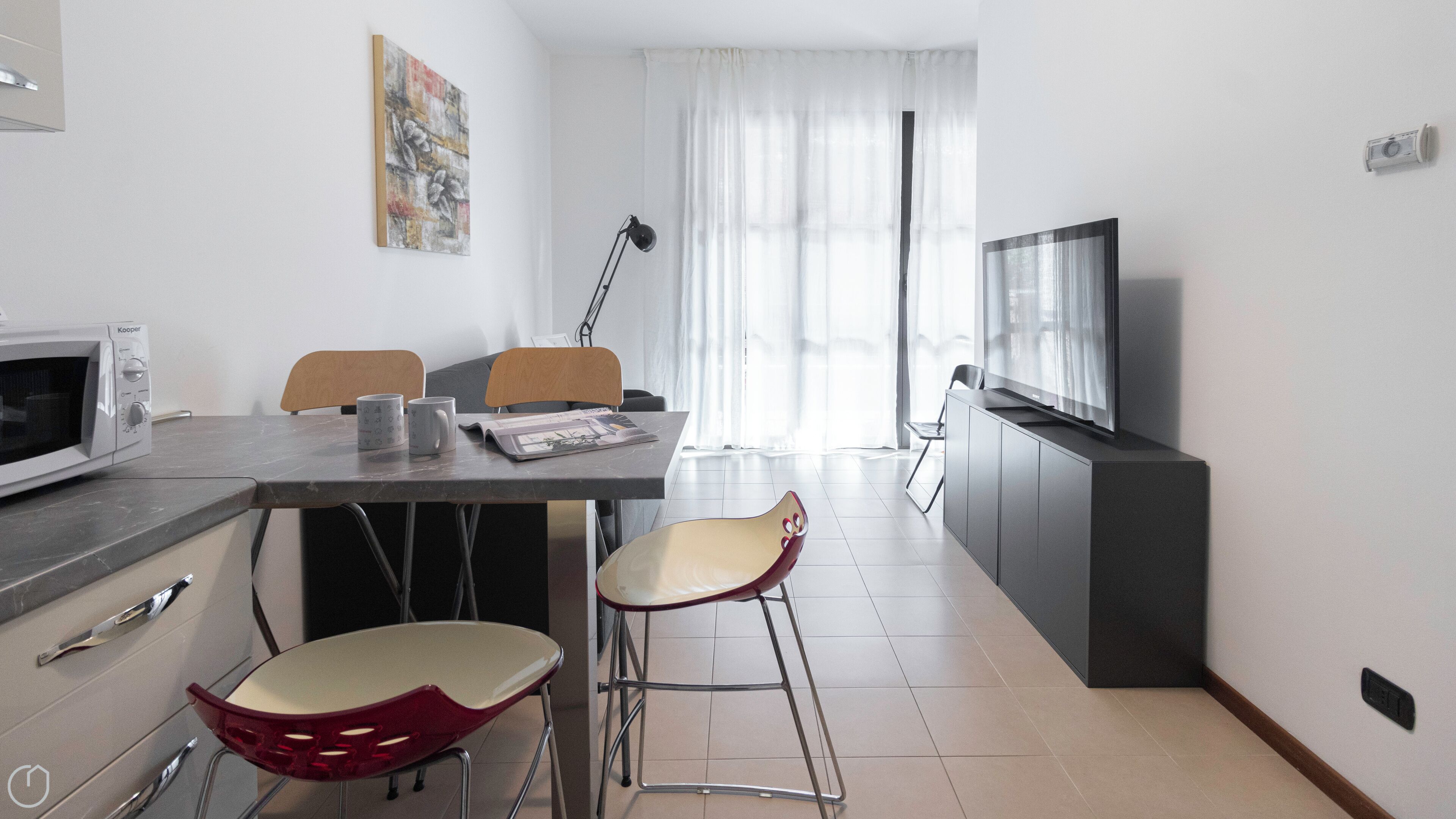 A modern kitchen with a microwave, two mugs, a magazine, and a red chair.