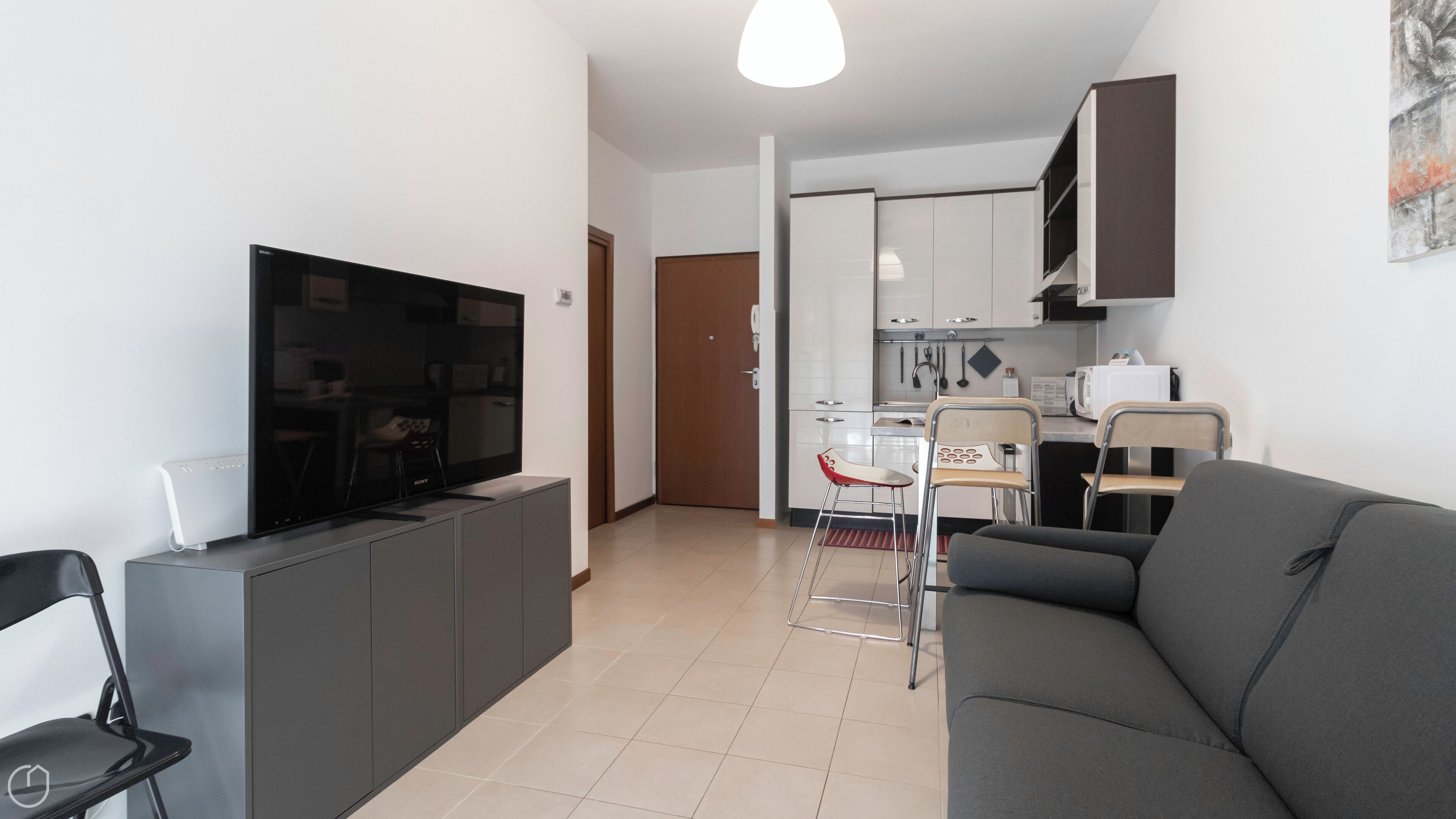 A modern living room with a flat-screen TV, a sofa, and a dining area with chairs and a table.