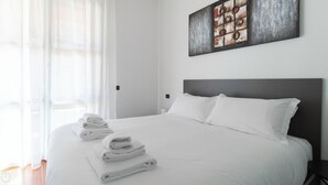 Cama bem arrumada com lençóis e toalhas brancas, cabeceira escura e uma obra de arte abstrata na parede.