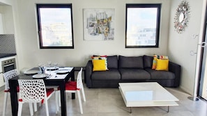 Een moderne woonkamer met een grijze bank, een eettafel met witte stoelen en een witte salontafel.