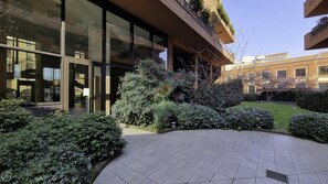 A modern building with large glass windows, a tiled courtyard, and well-maintained greenery. - Italianway Easy - Zuretti 32 (Milan)
