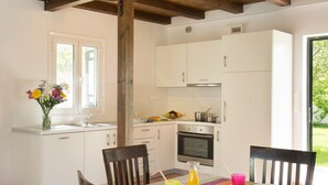 Une cuisine avec des meubles blancs, un plafond en bois et une table à manger avec des chaises.