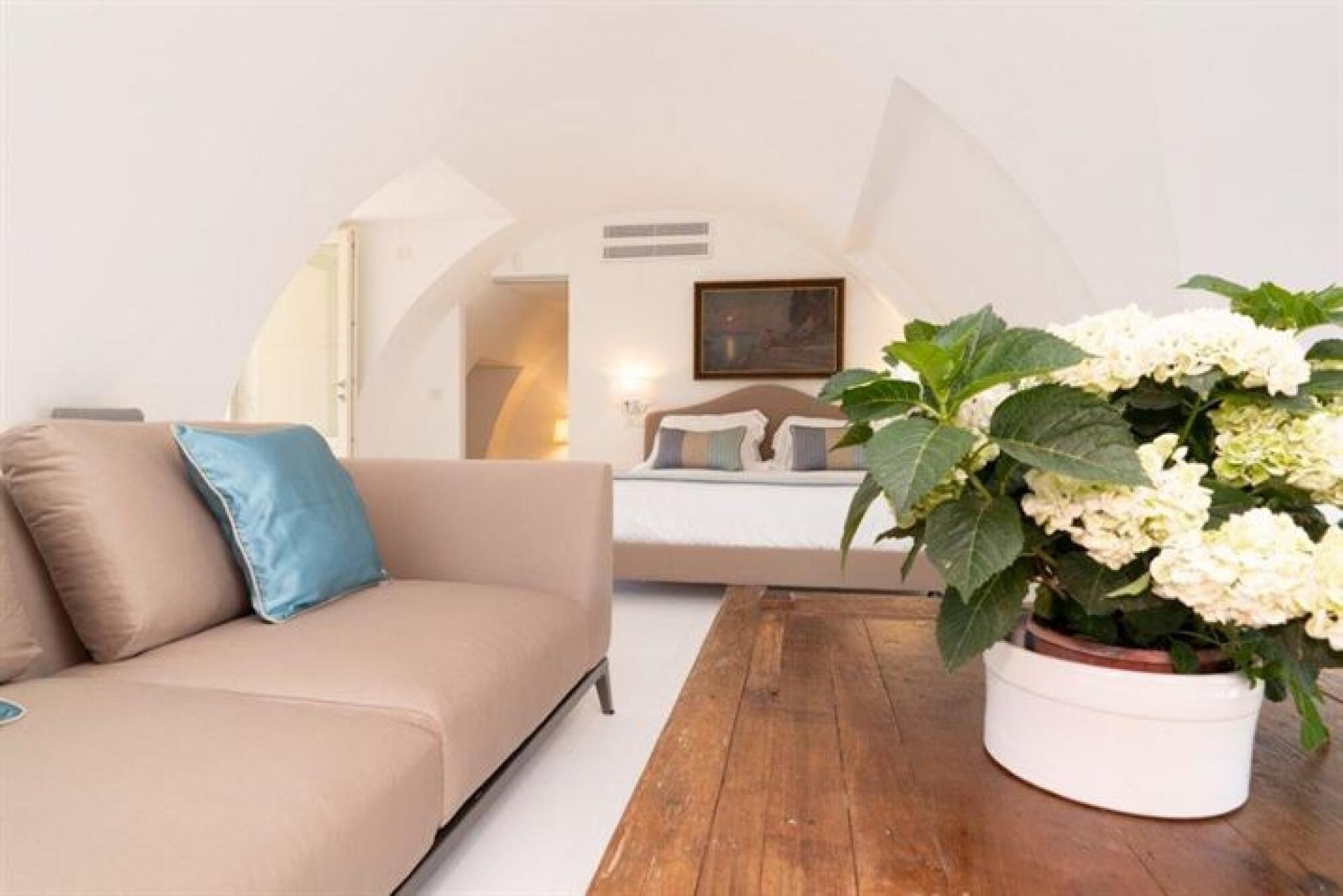 A cozy living room with a beige sofa, a wooden coffee table, and a potted plant with white flowers.