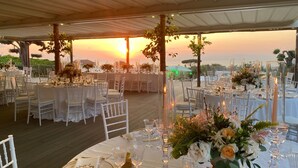 An outdoor wedding venue with round tables, white chairs, and floral centerpieces under a tent. - Villa Artemisia in Piano di Sorrento (Piano di Sorrento)