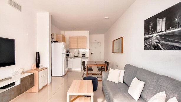 Un apartamento moderno con televisión de pantalla plana, comedor, cocina y sofá gris.