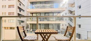 A balcony with a wooden table and two cushioned chairs, overlooking a multi-story residential building with balconies and windows. - Ben Yehuda Nuage in Tel Aviv-yafo (Tel Aviv)