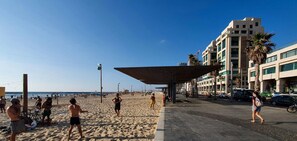 A beach with a covered seating area, a road with cars, and buildings in the background. - Ben Yehuda Nuage in Tel Aviv-yafo (Tel Aviv)