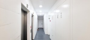 Un pasillo estrecho y bien iluminado con paredes blancas y piso de baldosas, que conduce a una puerta al final.