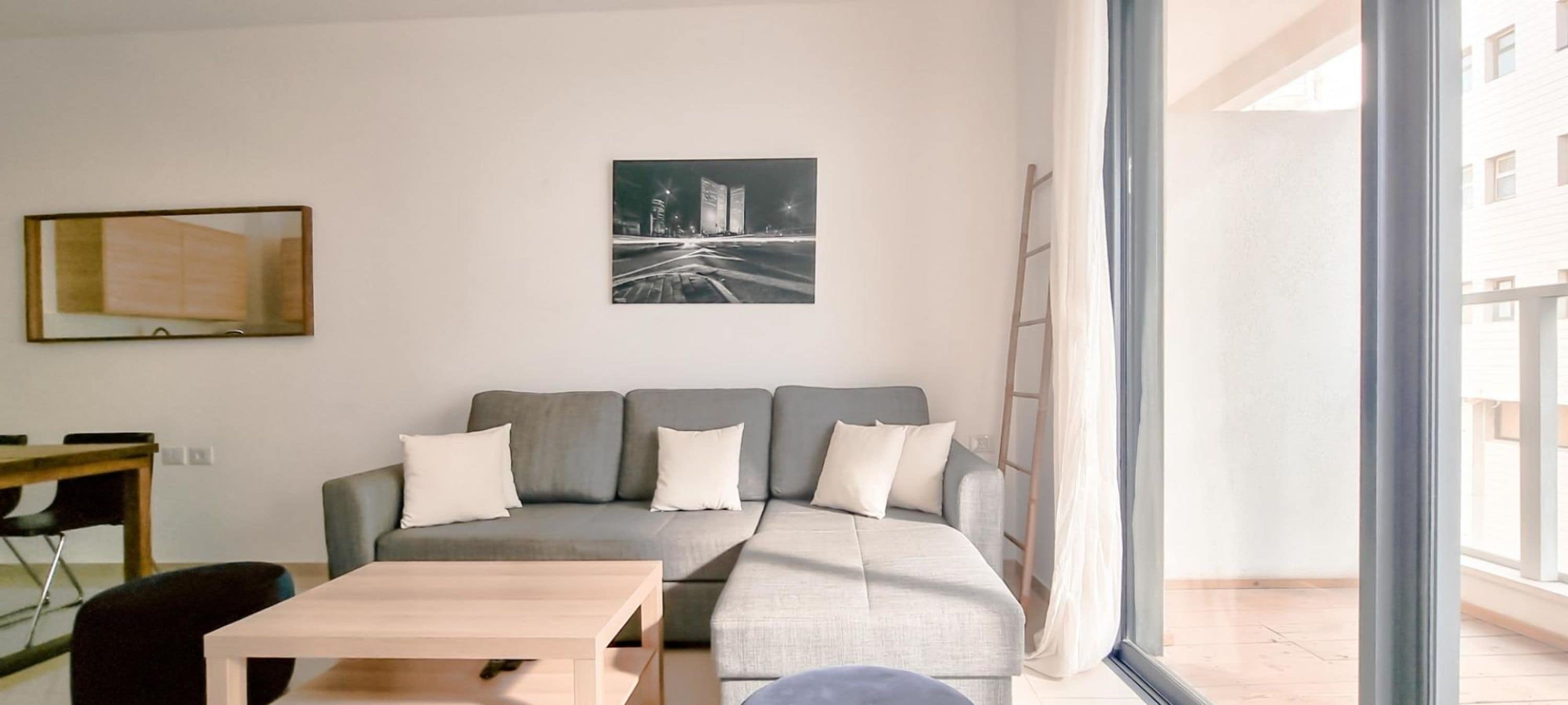 A modern living room with a grey sectional sofa, a wooden coffee table, and a framed picture on the wall.