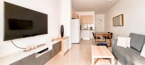 Ein modernes Wohnzimmer mit Flachbildfernseher, einer Couch, einem Esstisch und einer Küche im Hintergrund.