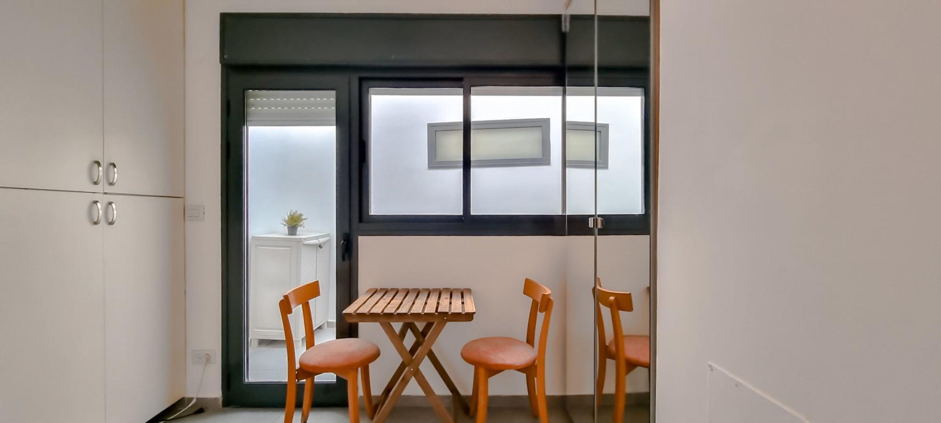 A small room with a wooden table and two chairs, a window with frosted glass, and a radiator.