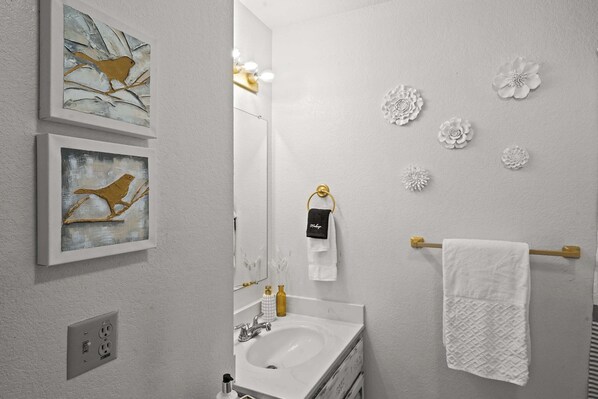 A bathroom with a white sink, a mirror, and a towel rack. There are two framed paintings on the wall. - Cozy PC Condo Top Floor Studio (Park City)