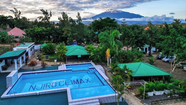 Una piscina con la inscripción "Njiro Climax", rodeada de exuberante vegetación y una montaña al fondo.