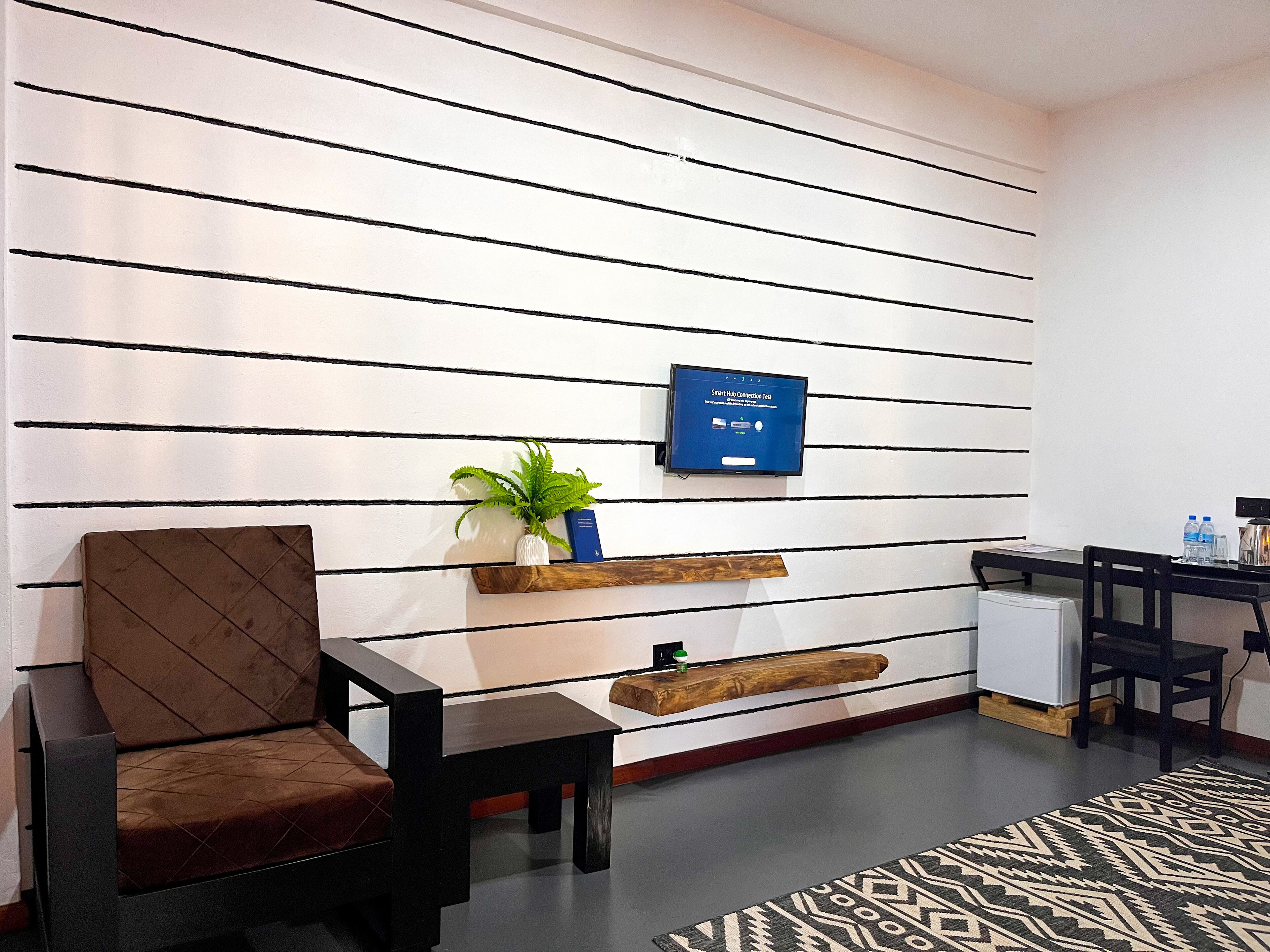 Ein moderner Empfangsbereich mit einer Couch, einem kleinen Tisch, einer Zimmerpflanze, einem Wandfernseher und einem Holzregal.