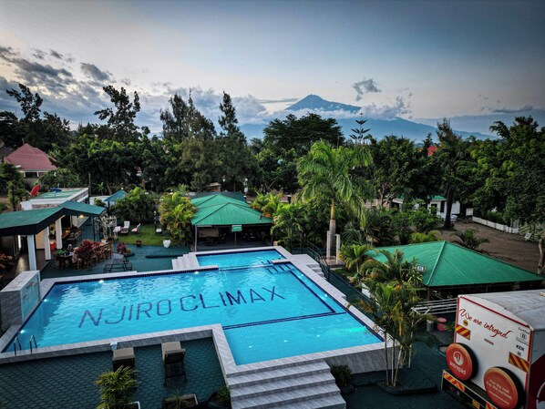 Uma piscina com a inscrição 'NJIRO CLIMAX' na água, rodeada por vegetação exuberante e uma montanha ao fundo.